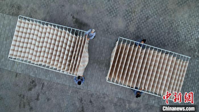 中国侨网8月29日，河北省衡水市冀州区田园棉文化园纺织工坊，工人整理晾晒中的老粗布。该文化园依托当地传统“非遗”田园棉手织布技艺，引导帮扶周边农户学习手织老粗布，让农户实现家门口就业增收，推进传统手工艺的传承和发展。2013年，冀州田园棉手织布技艺入选河北省级非物质文化遗产名录。（无人机照片）中新社记者 翟羽佳 摄